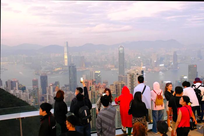 A crowd gazes out over a city skyline under an overcast sky.