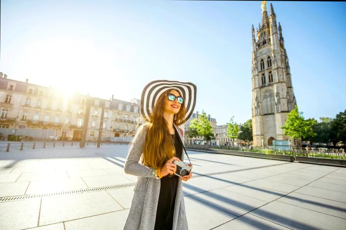 A young female traveler capturing moments with her camera in Pey-Berland square, featuring the bell tower in the backdrop of Bordeaux.