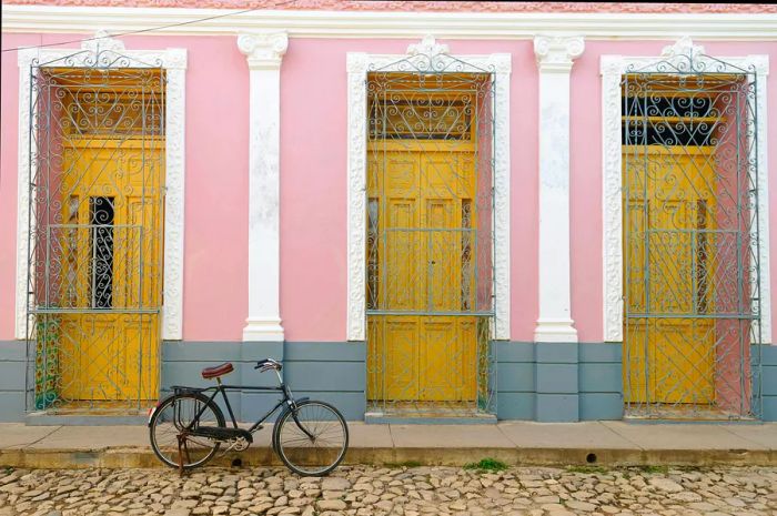 A typical pastel-colored house with wooden doors framed by decorative plaster and wrought-iron grills, located in Trinidad.