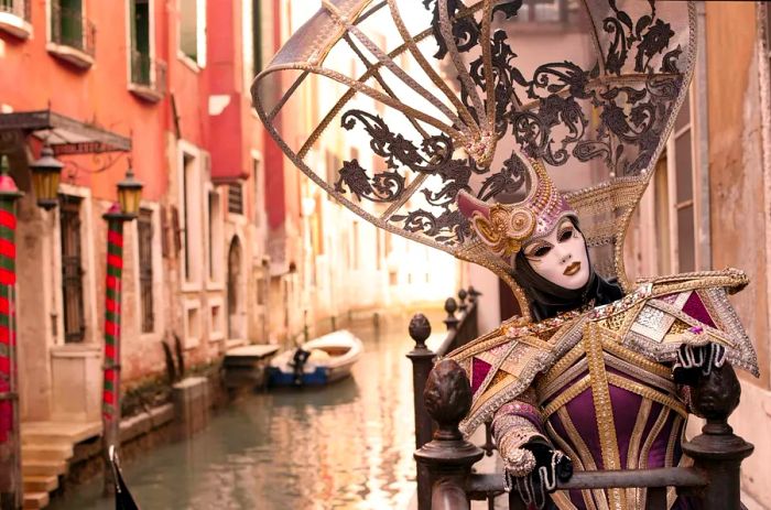 A masked reveler during the Venice Carnival, posing in front of a canal-side house in Venice, Italy.