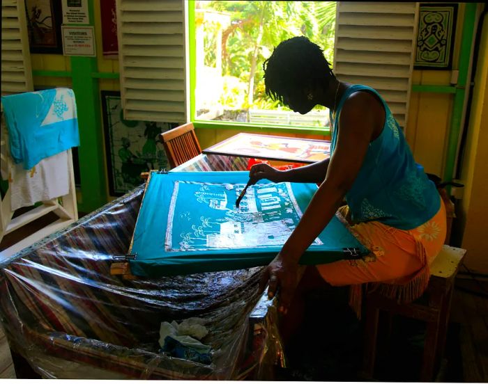 A woman creates art on a piece of turquoise fabric stretched over a frame