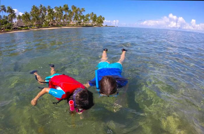 A mother and child enjoy snorkeling over a vibrant coral reef at a tropical resort.