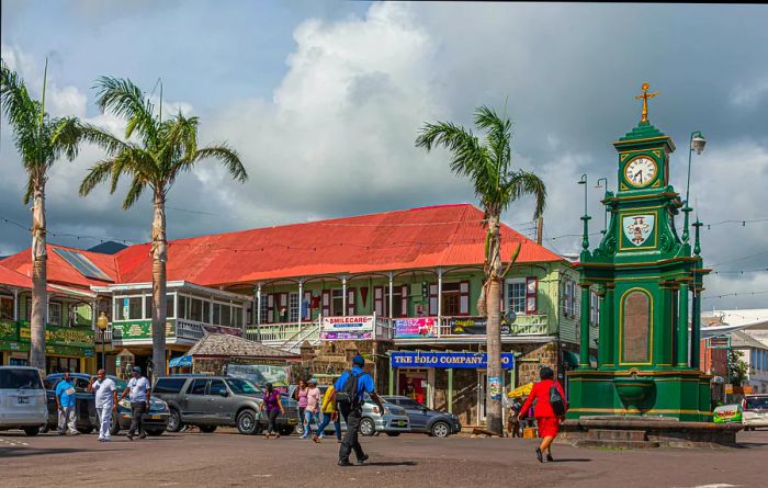 A small green clock tower is positioned at a road junction in a town