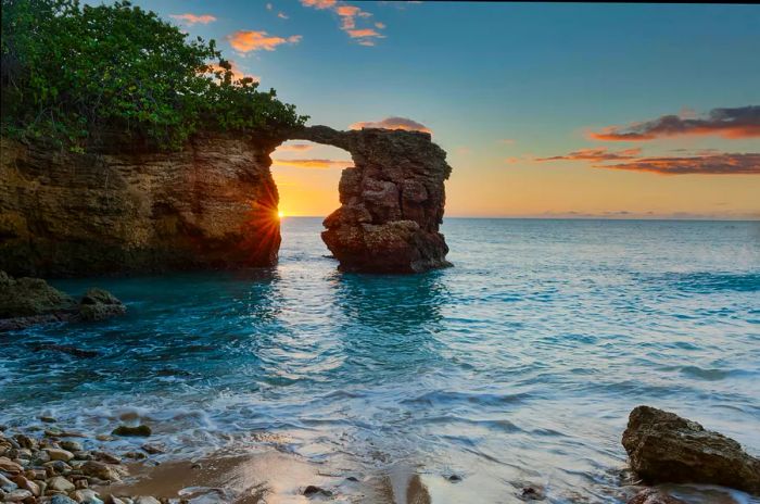 Witness the sunset framed by the natural rock bridge near Cabo Rojo Lighthouse, Puerto Rico.