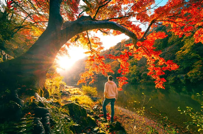 A man gazes across the Katsura River while perched on a smooth rock, framed by autumn leaves.