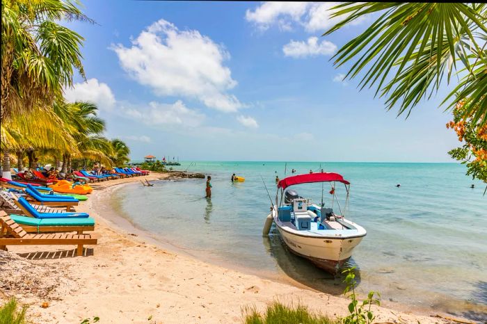 Lounge chairs, a woman in a bikini splashing in the water, and a boat anchored just offshore