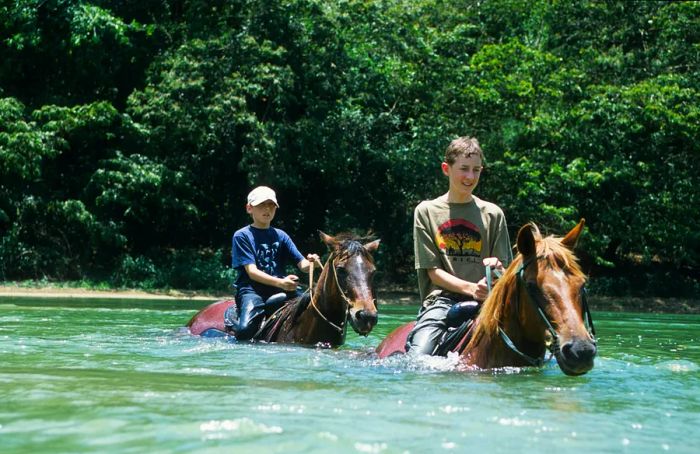 Children riding horses through a river