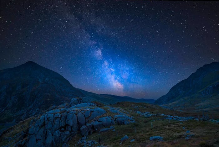 A breathtaking composite image of the vibrant Milky Way over a dramatic valley landscape in Wales.