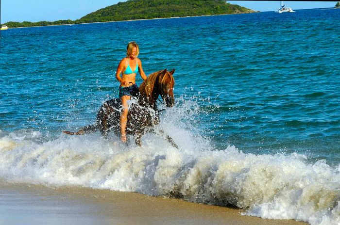 A woman beams as she rides a horse through the crashing waves on a beach.