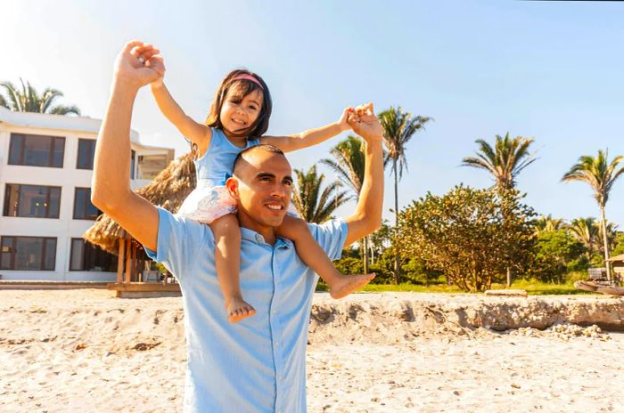 A father carries his daughter on his shoulders along the beach in Honduras