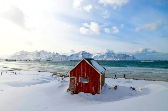 The striking red Rorbuer hut at the renowned Rambergstranda beach on Lofoten island, Norway, is blanketed in snow.