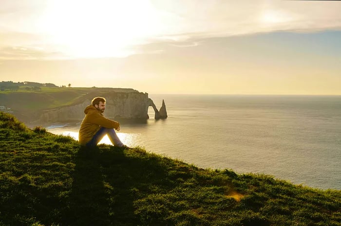 A wide-angle view captures a man admiring the cliffs of Etretat at sunset.