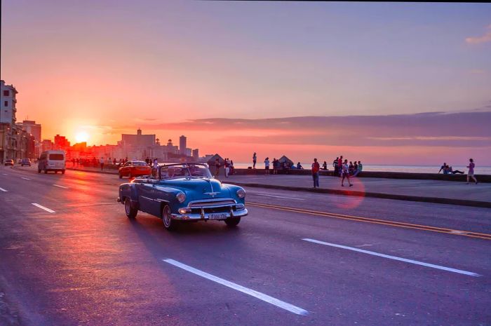 A vintage car cruises along Havana's coastal road as the sun sets.