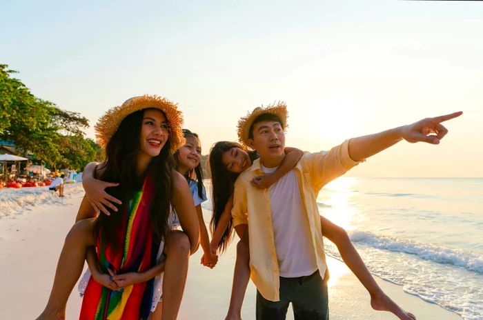 A family enjoying their summer beach vacation, with kids on shoulders as the father points at something in the distance