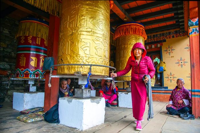 An elderly woman turning a large prayer wheel at the National Memorial Chorten complex in Thimphu, Bhutan