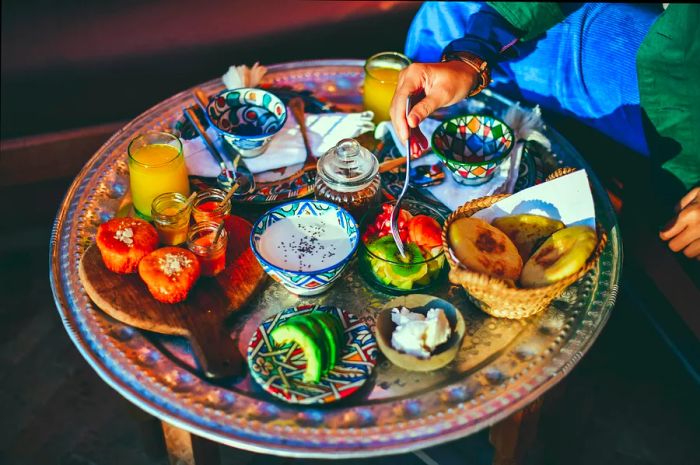 A Moroccan breakfast spread featuring fresh juice, fruits, muffins, honey, yogurt, and avocado.