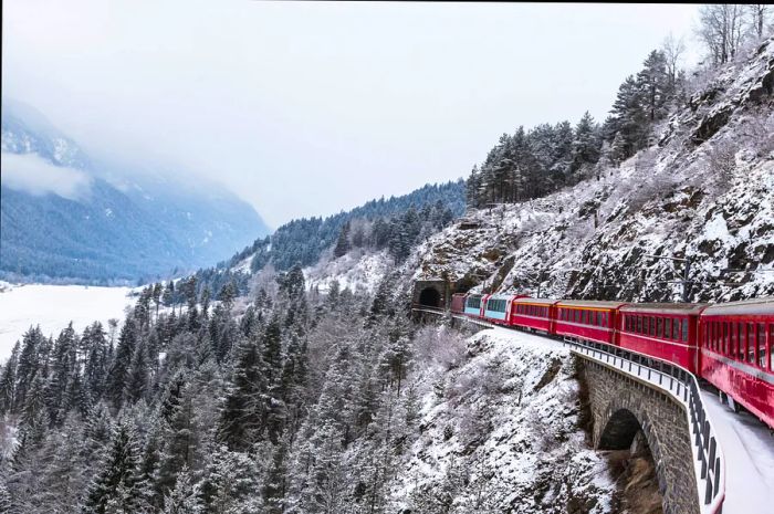 A train passes through a tunnel amidst a snowy landscape in Switzerland.