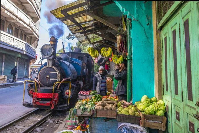 The Darjeeling Himalayan Railway winds through the town of Ghum, West Bengal, India, passing by local produce vendors.