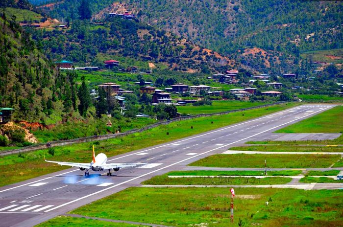 An airplane descends onto a runway flanked by steep green hills.