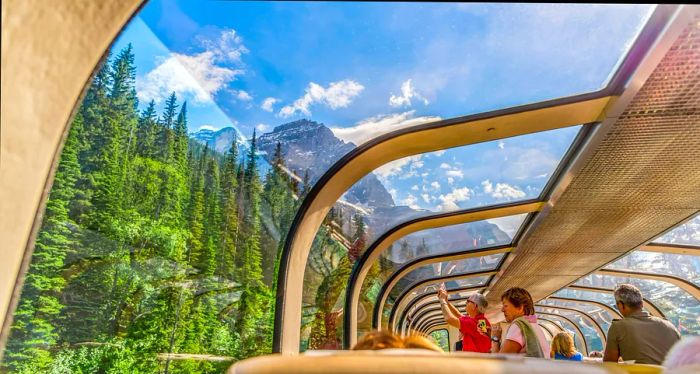 Passengers enjoy the view from the observation deck of a train as it travels through the Rocky Mountains.