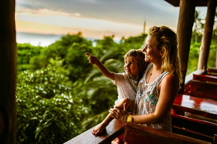 A small boy in his mother’s arms beams as he points towards the lush jungle surroundings from their balcony.