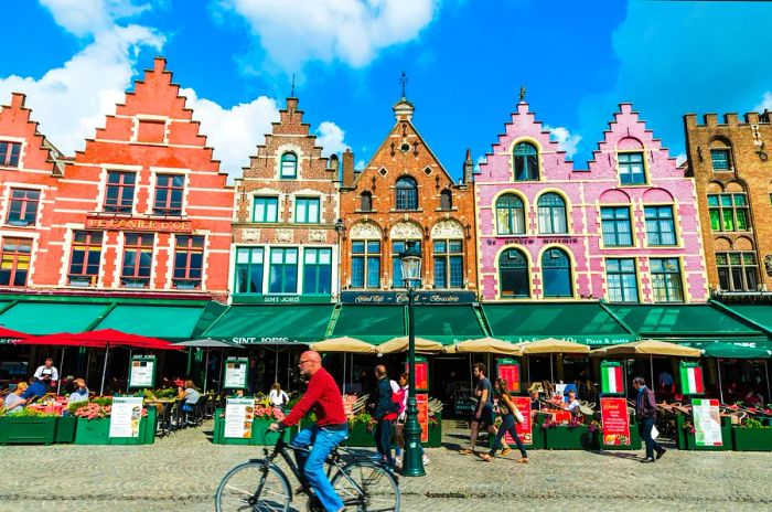 Pastel-hued tall buildings encircle a square bustling with cafes and restaurants below. A cyclist zooms by.