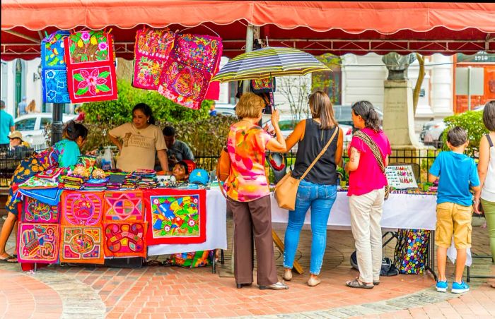 A group of travelers browses tables brimming with souvenirs at an outdoor market in Panama City, Panama.