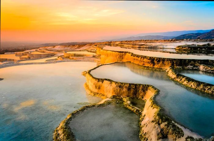 A series of bright white, tiered travertine formations bathed in the golden light of sunset