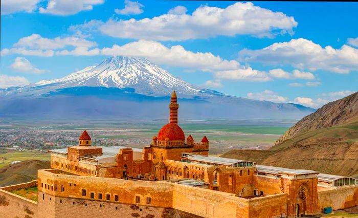 A red-stone palace featuring a central domed tower, with a snow-capped mountain looming in the background.