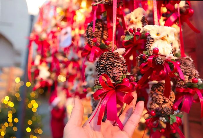 A hand grasping a pinecone adorned with a red ribbon.