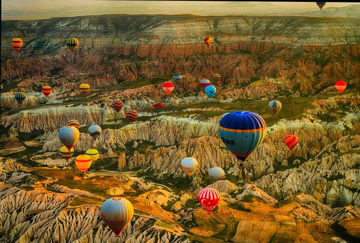 Aerial view of vibrant hot-air balloons floating over a landscape filled with hills and unique rock formations