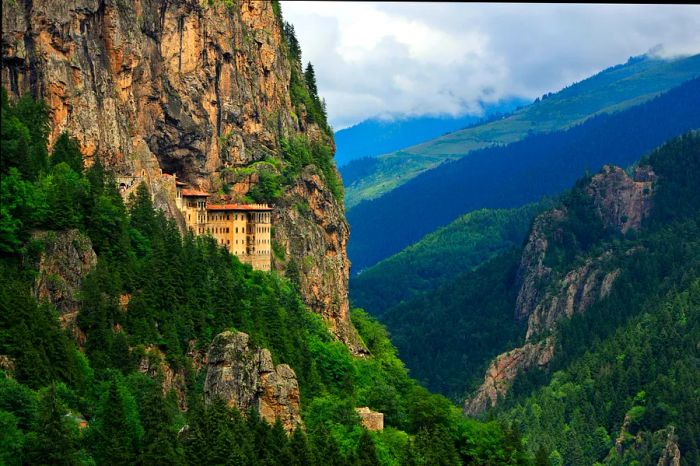 A monastery carved into the face of a towering cliff overlooking a valley