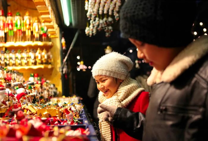 Two children bundled up in warm clothes admire the festive ornaments for sale at a Christmas market.