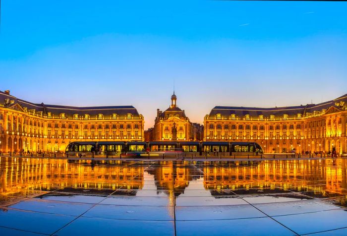 A tram glides past the stunning Place de la Bourse, beautifully illuminated and reflected in the water fountain below.