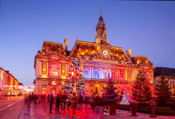 A stunning Renaissance-style structure radiating in various colors, adorned with numerous illuminated Christmas trees in its front garden.