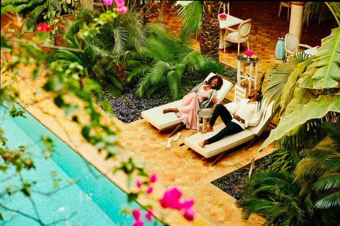 Wide high-angle shot of a couple lounging by the pool in the courtyard of a luxury hotel during their vacation