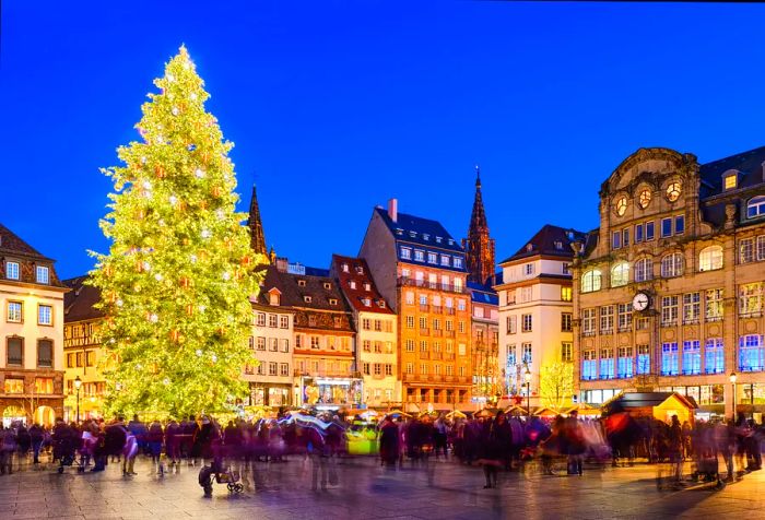 A radiant Christmas tree stands tall above a plaza bustling with visitors.