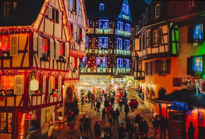 Crowds gather in the streets, surrounded by traditional half-timbered houses adorned with vibrant lights and festive decorations.