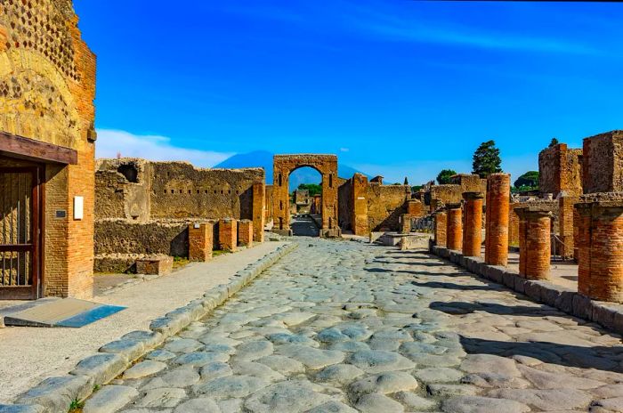 The ruins of Pompeii set against a vibrant blue sky, with Mt Vesuvius looming in the background