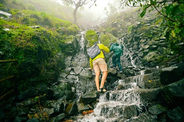 A father and teenager assist each other as they trek over flooded rocks in India.