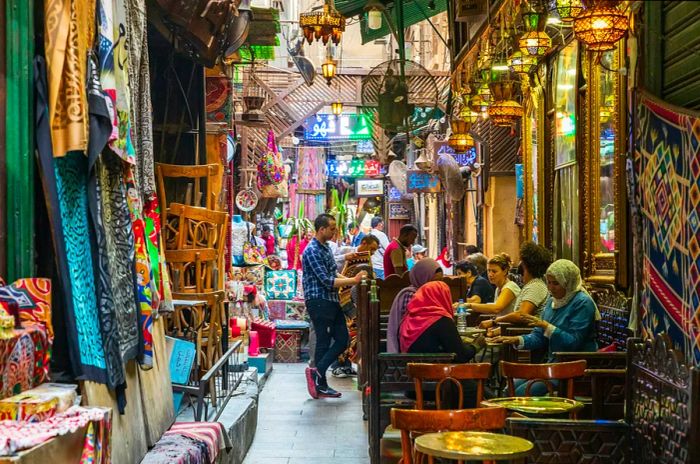 People gather at tables outside a bustling coffee shop in a lively souk