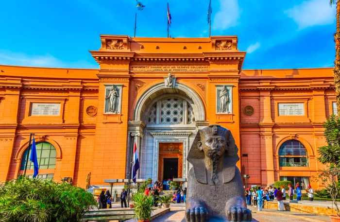 A sphinx perched outside a charming salmon-pink historic building in a bustling city square