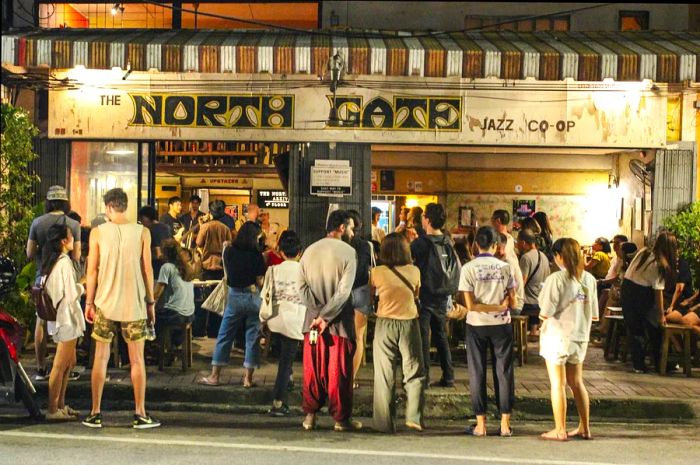 A lively crowd gathers at the North Gate Jazz Co-Op bar to enjoy live music, with people spilling outside onto the pavement.