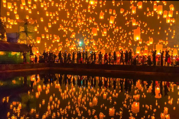 Festival attendees admiring the Sky Lanterns Firework Festival in Chiang Mai, with the lanterns reflecting on the water.