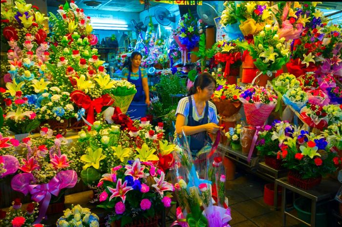 A worker in a blue apron tends to the vibrant blooms at the Pak Khlong Flower Market.