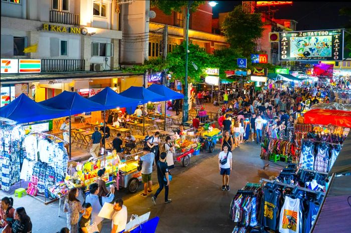 Vendors are selling food, clothing, and drinks at the Khao San Road night market, where tourists and locals mingle among the stalls.