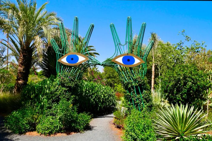 Two large hand sculptures with blue eyes stand guard along a pathway in a botanical garden.