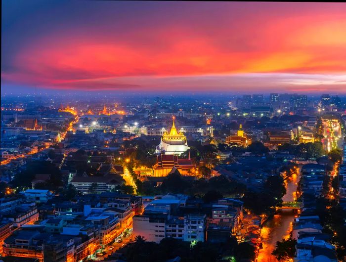 Wat Saket, known as the Golden Mount, glows brilliantly at dusk, overlooking the Bangkok skyline bathed in a warm peach and orange sunset.