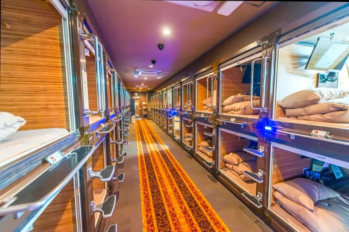 A long hallway features recessed sleeping pods on either side at a capsule hotel in Japan.