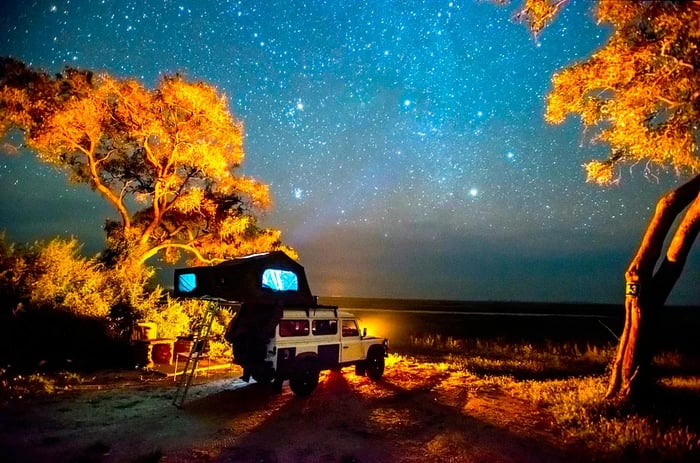 Beneath a sky full of stars, a 4WD camping vehicle is parked beside a tree in Chobe National Park, Botswana.